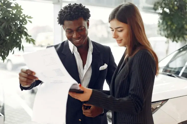 How can I sell my car – professional agent helping a customer review car sale documents at a dealership.