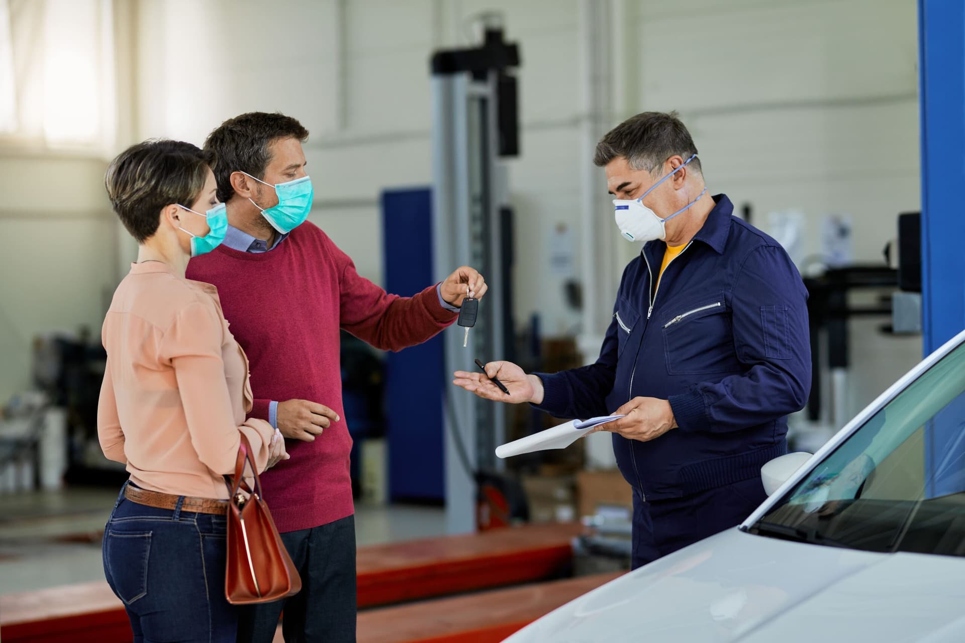 Selling a car before MOT expiry as owner hands over car keys to buyer at auto service center.